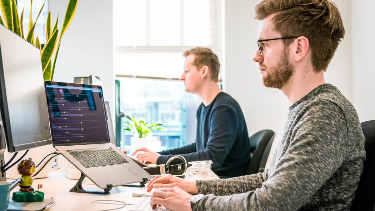 Zwei Personen arbeiten am Schreibtisch vor zwei Monitoren.