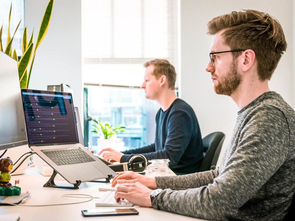 Zwei Personen arbeiten am Schreibtisch vor zwei Monitoren.